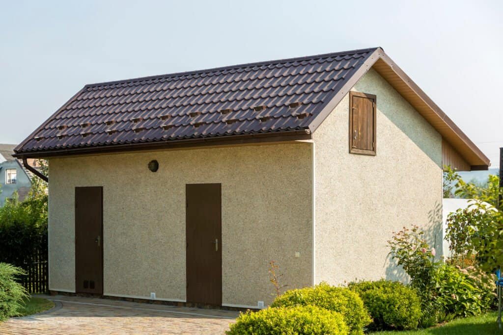 Small building with a tiled roof and two doors, surrounded by greenery.